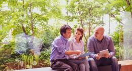 A man pointing to a document heald by a woman with another man next to her holding a tablet