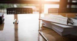 Picture of a desk with a pile of documents, a pencil and glasses