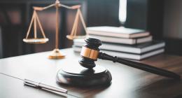 A gavel resting on a desk with scales and books in the background